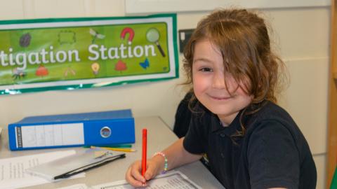 A pupil writing in her notebook looks up for the camera